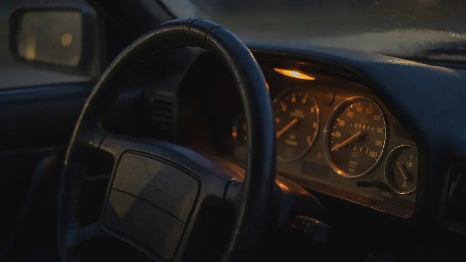 Leather steering wheel and warm-lit dashboard gauges inside a dark car cabin.